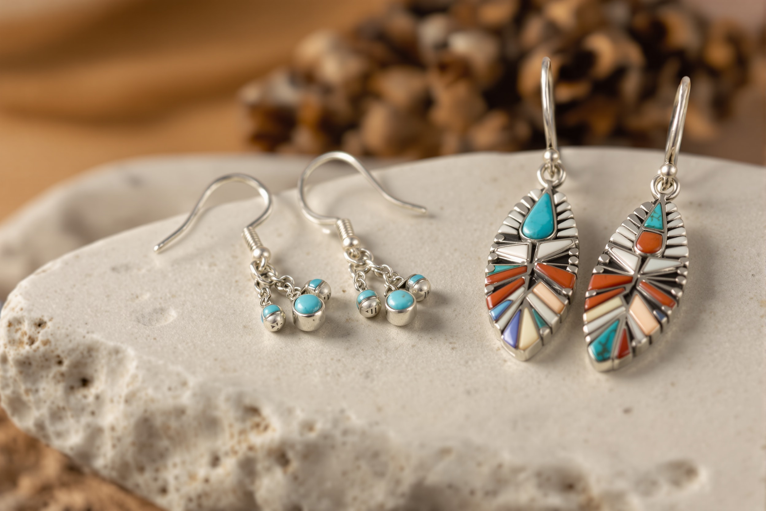 Silver turquoise dangle earrings beside Zuni inlay earrings on pale stone