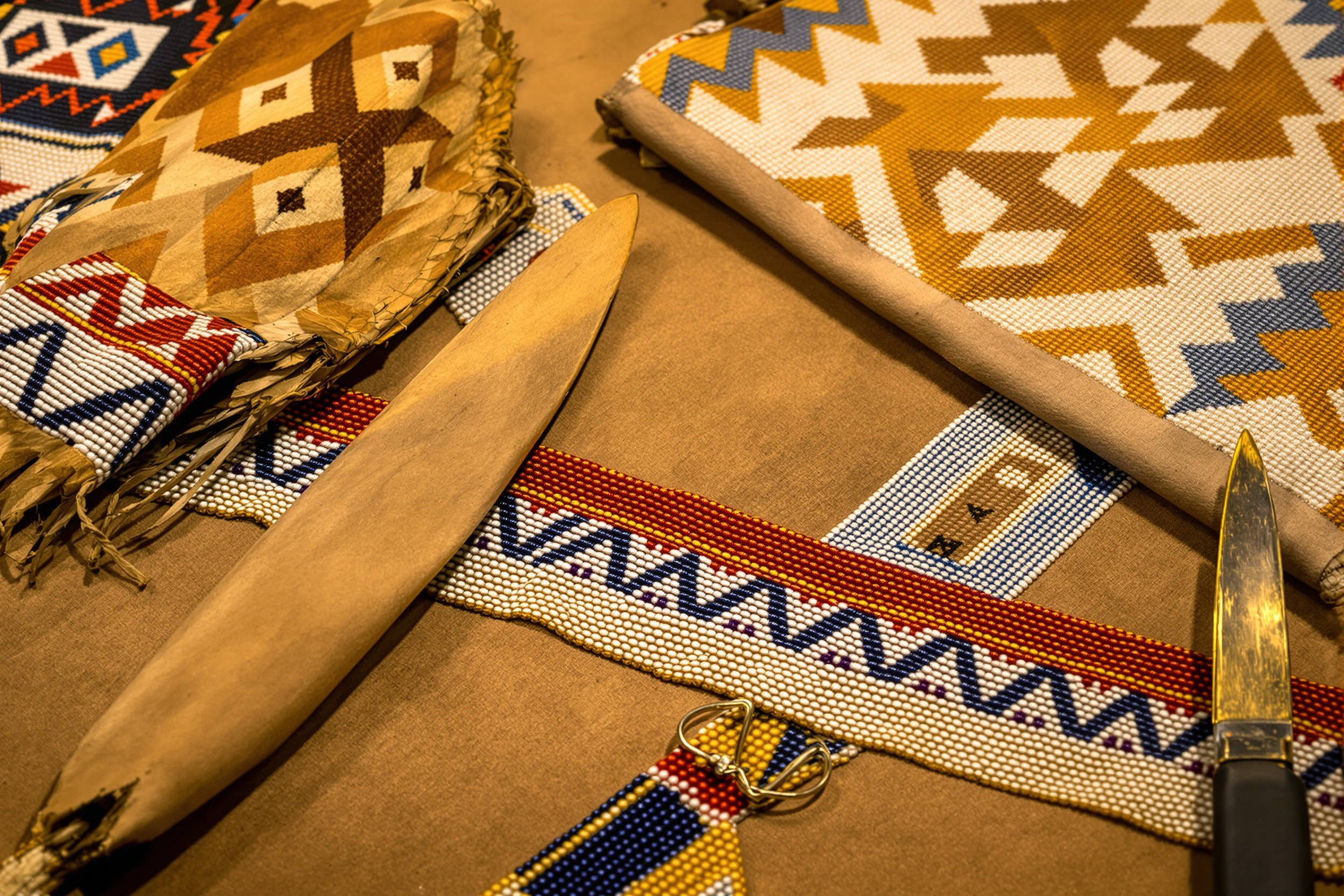 Plains geometric glass seed beadwork on hide beside a painted rawhide parfleche